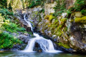 A stunning waterfall cascades down rocky cliffs in Glacier National Park, surrounded by lush greenery.