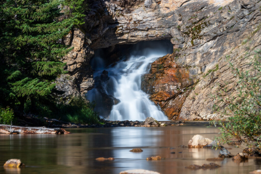 Waterfall flowing from a cave with reflection in water.