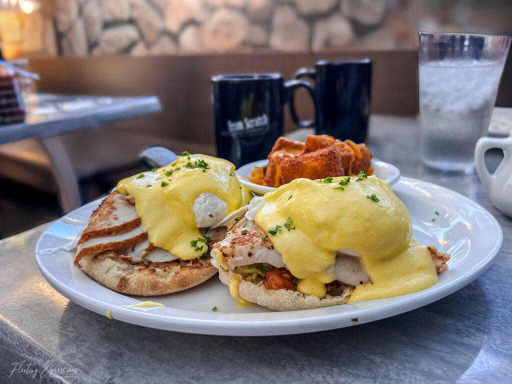 eggs benedict plated and sitting on Eggs Benedict is plated and sitting on a table with a glass of water and a coffee cup.